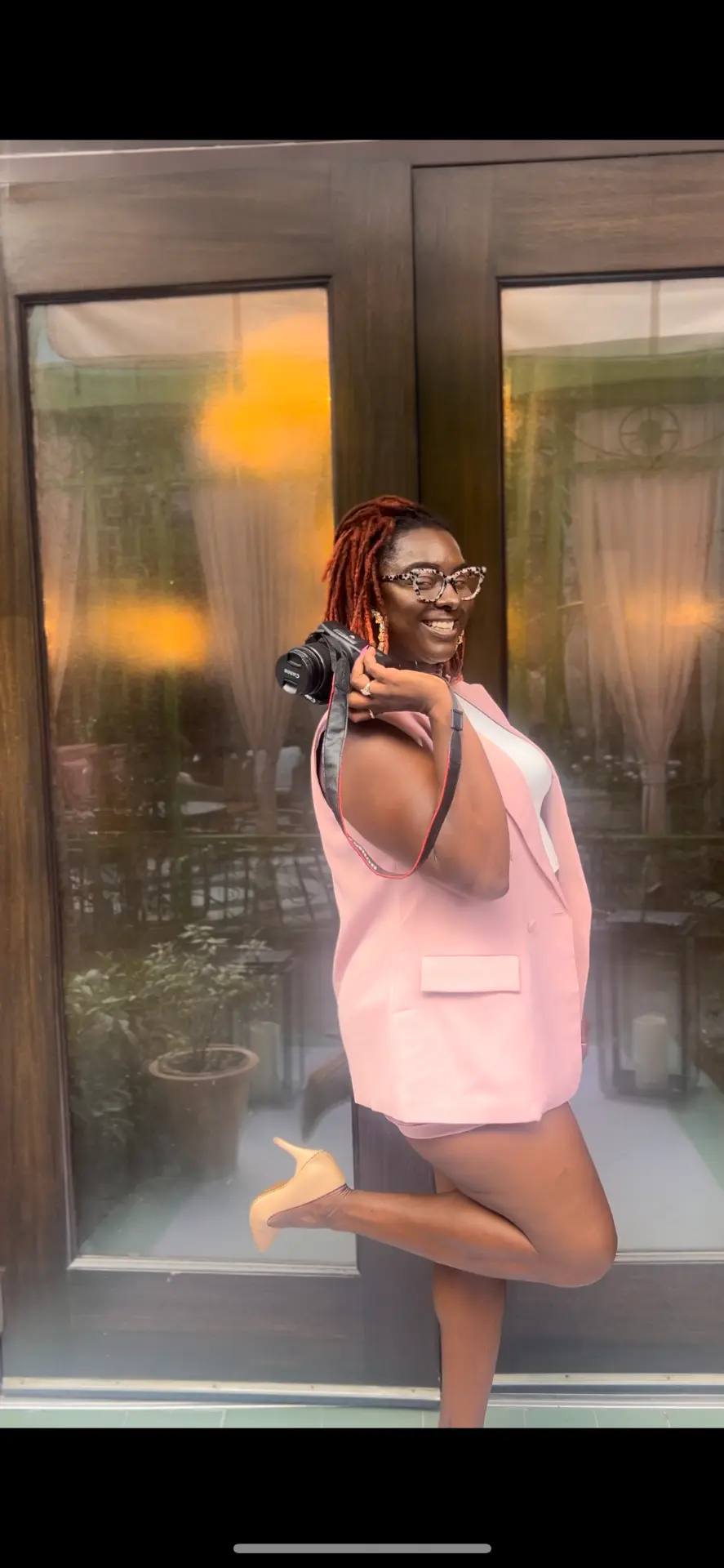 Antwonette standing outside a restaurant entrance with a camera over her shoulder