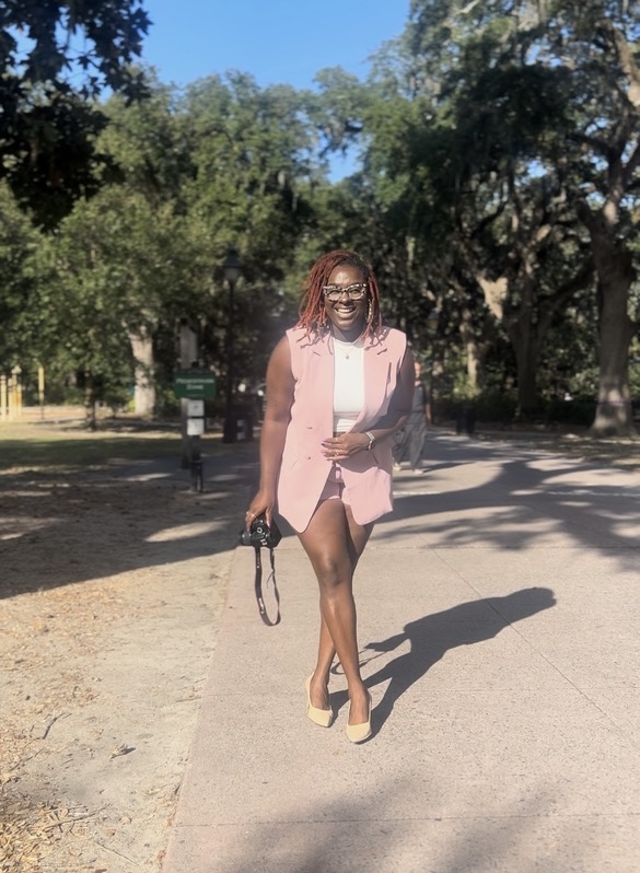 Antwonette walking through a tree-lined Savannah square with a camera in hand